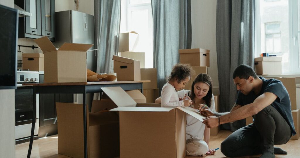 Parents with daughter packing and writing on boxes to move.